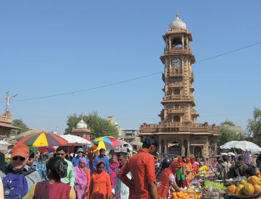 Shoppers, fruit stalls and bright umbrellas in Sardar Market with Ghanta Ghar beyond.